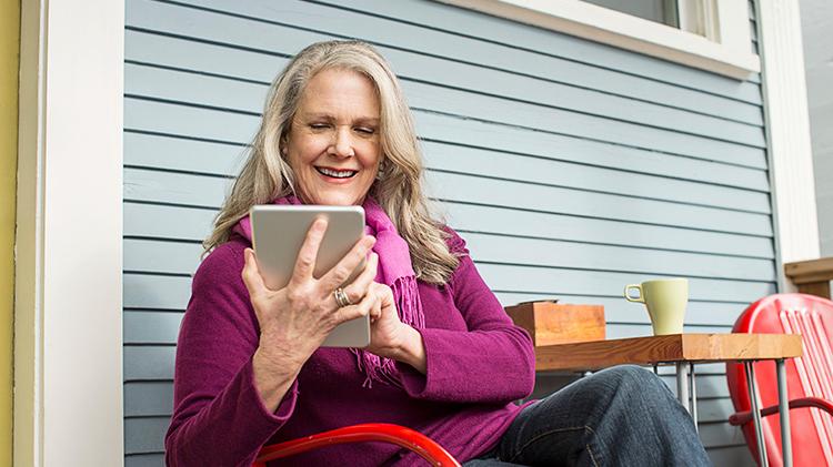 A woman sitting outside and reading about borrowing against a life insurance policy on her tablet.